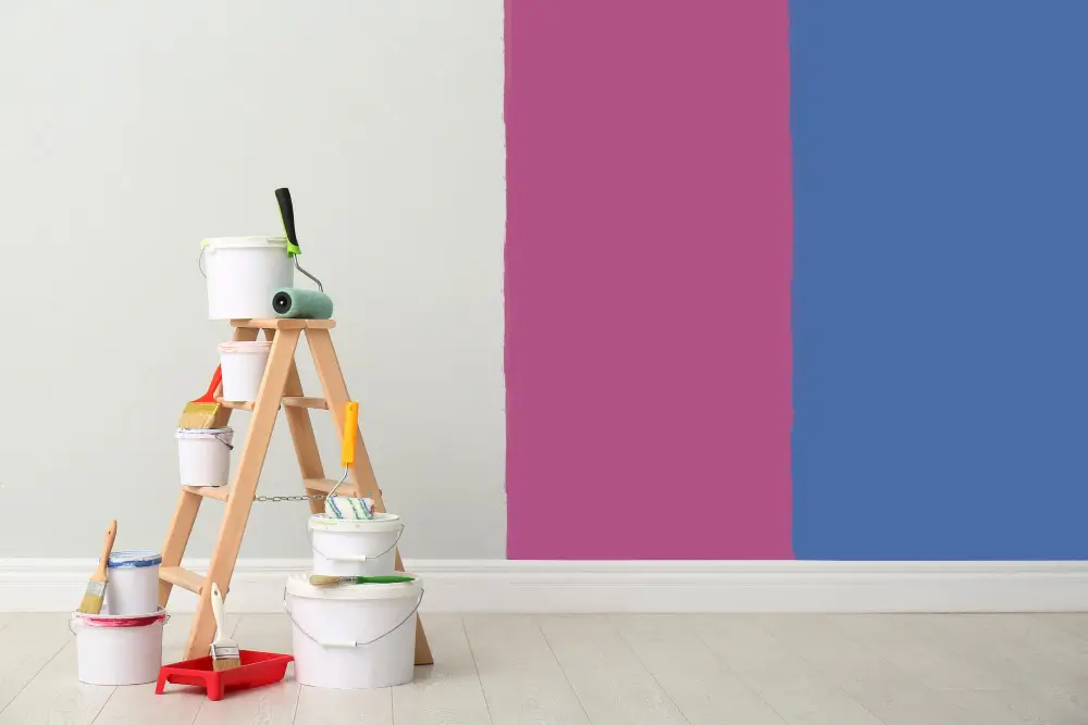Amore Painters color samples on a wall with brushes and tools on the ground.