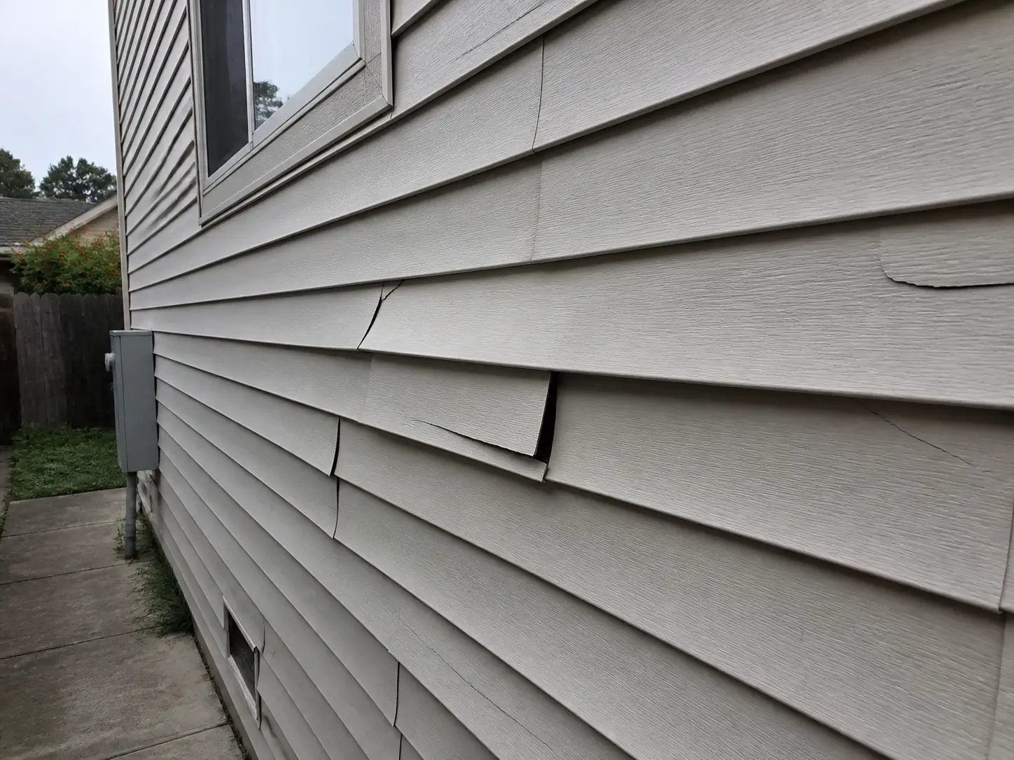 Cracked and buckled vinyl siding panels that need replacement rather than a new coat of paint.
