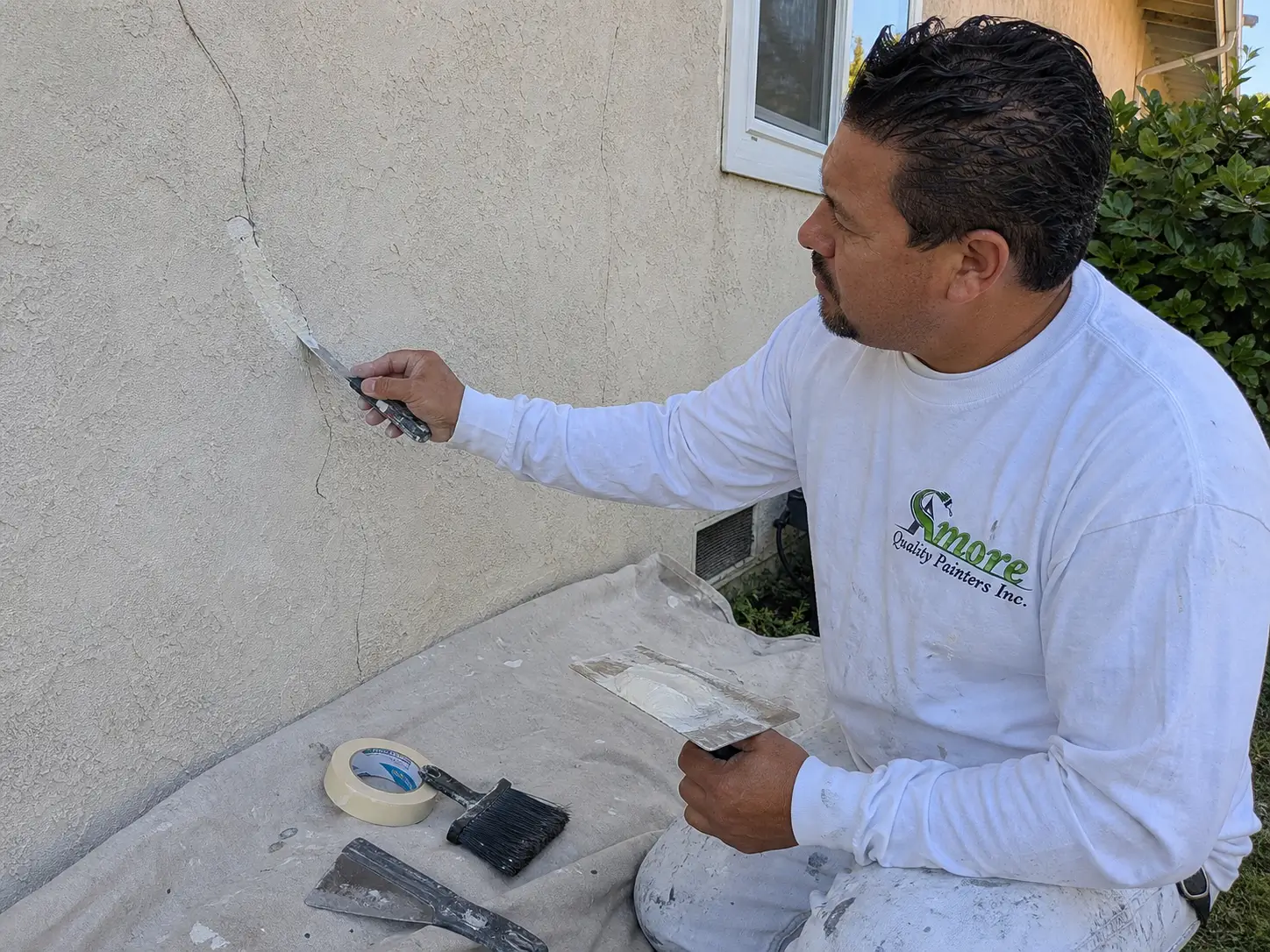 Amore Painters contractor repairs a crack in an exterior stucco wall before painting.