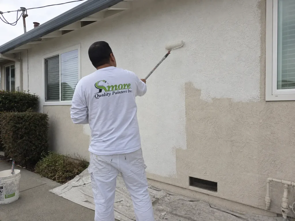 Amore Painters contractor back-rolls white paint onto the textured stucco exterior of a California home.